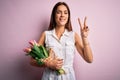 Young beautiful brunette woman holding bouquet of tulips flowers over pink background smiling with happy face winking at the Royalty Free Stock Photo