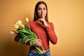 Young beautiful brunette woman holding bouquet of tulips flowers over yellow background asking to be quiet with finger on lips Royalty Free Stock Photo