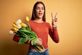 Young beautiful brunette woman holding bouquet of tulips flowers over yellow background smiling with happy face winking at the Royalty Free Stock Photo