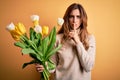 Young beautiful brunette woman holding bouquet of yellow tulips over  background asking to be quiet with finger on lips Royalty Free Stock Photo