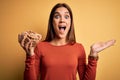 Young beautiful brunette woman holding bowl with cornflakes cereals over yellow background very happy and excited, winner