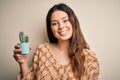 Young beautiful brunette woman holding cactus pot over isolated white background with a happy face standing and smiling with a Royalty Free Stock Photo