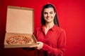 Young beautiful brunette woman holding delivery box with Italian pizza over red background with a happy face standing and smiling Royalty Free Stock Photo