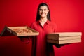 Young beautiful brunette woman holding delivery boxes with Italian pizza over red background with a happy face standing and Royalty Free Stock Photo