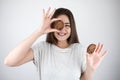 Young beautiful brunette woman holding one chocolate cookie near her eye showing ok sign healthy lifestyle isolated white