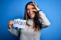 Young beautiful brunette woman holding paper with brexit message over blue background with happy face smiling doing ok sign with Royalty Free Stock Photo