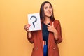 Young beautiful brunette woman holding paper with question mark smiling happy pointing with hand and finger Royalty Free Stock Photo