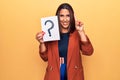 Young beautiful brunette woman holding paper with question mark smiling with an idea or question pointing finger with happy face, Royalty Free Stock Photo