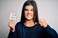 Young beautiful brunette woman holding paper with reminder paper with tax day message annoyed and frustrated shouting with anger,