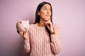 Young beautiful brunette woman holding piggy bank saving money for retirement serious face thinking about question, very confused Royalty Free Stock Photo