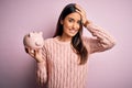 Young beautiful brunette woman holding piggy bank saving money for retirement stressed with hand on head, shocked with shame and Royalty Free Stock Photo