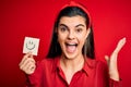 Young beautiful brunette woman holding reminder paper with smile emoji message very happy and excited, winner expression Royalty Free Stock Photo