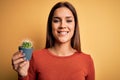 Young beautiful brunette woman holding small cactus pot over yellow background with a happy face standing and smiling with a Royalty Free Stock Photo