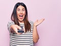 Young beautiful brunette woman holding television remote control over pink background celebrating achievement with happy smile and Royalty Free Stock Photo