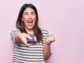 Young beautiful brunette woman holding television remote control over pink background screaming proud, celebrating victory and Royalty Free Stock Photo