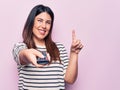 Young beautiful brunette woman holding television remote control over pink background smiling with an idea or question pointing Royalty Free Stock Photo