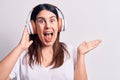 Young beautiful brunette woman listening to music using headphones over white background celebrating achievement with happy smile Royalty Free Stock Photo