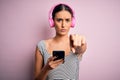 Young beautiful brunette woman listening to music using headphones and smartphone pointing with finger to the camera and to you, Royalty Free Stock Photo