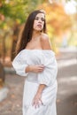 Beautiful young woman in a long white dress with dark brown hair posing outdoors on a blurred background. Royalty Free Stock Photo