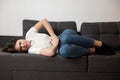 Young beautiful brunette woman lying on the sofa suffering from extreme pain in stomach during periods looking desperate, Royalty Free Stock Photo