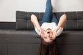 Young beautiful brunette woman lying on the sofa upside down in her appartment, grimacing, having fun, feeling cozy and happy at Royalty Free Stock Photo