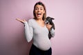 Young beautiful brunette woman pregnant expecting baby holding chihuahua puppy very happy and excited, winner expression