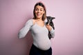 Young beautiful brunette woman pregnant expecting baby holding chihuahua puppy very happy pointing with hand and finger