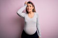 Young beautiful brunette woman pregnant expecting baby over isolated pink background confuse and wonder about question