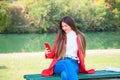 Young beautiful brunette woman with red lips and long straight hair wearing red jacket sitting outdoor in autumn park. Royalty Free Stock Photo