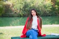 Young beautiful brunette woman with red lips and long straight hair wearing red jacket sitting outdoor in autumn park. Royalty Free Stock Photo