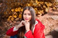 Young beautiful brunette woman with red lips and long straight hair wearing red jacket sitting outdoor in autumn park. Royalty Free Stock Photo