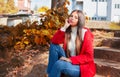 Young beautiful brunette woman with red lips and long straight hair wearing red jacket sitting outdoor in autumn park. Royalty Free Stock Photo