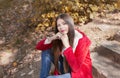 Young beautiful brunette woman with red lips and long straight hair wearing red jacket sitting outdoor in autumn park. Royalty Free Stock Photo