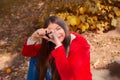 Young beautiful brunette woman with red lips and long straight hair wearing red jacket sitting outdoor in autumn park. Royalty Free Stock Photo