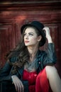 Young beautiful brunette woman with red short dress and black hat posing sensual in vintage scenery. Romantic mysterious lady Royalty Free Stock Photo