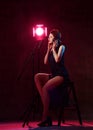 Young beautiful brunette woman with short hair in elegant black dress and shoes sitting in studio in headphones and singing