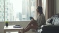 Young beautiful brunette woman sits on the sofa puts her feet on table and relaxes. The girl watches TV by the window Royalty Free Stock Photo