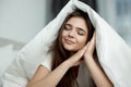 Young beautiful brunette woman sitting in bed with blanket on her head with her hands near her face in the morning Royalty Free Stock Photo