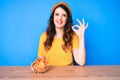 Young beautiful brunette woman sitting on the table eating nachos potato chips doing ok sign with fingers, smiling friendly Royalty Free Stock Photo