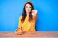 Young beautiful brunette woman sitting on the table eating nachos potato chips pointing with finger to the camera and to you, Royalty Free Stock Photo