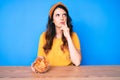 Young beautiful brunette woman sitting on the table eating nachos potato chips serious face thinking about question with hand on Royalty Free Stock Photo