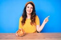 Young beautiful brunette woman sitting on the table eating nachos potato chips smiling happy pointing with hand and finger to the Royalty Free Stock Photo