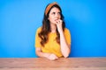 Young beautiful brunette woman sitting on the table over blue background looking stressed and nervous with hands on mouth biting Royalty Free Stock Photo