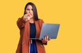 Young beautiful brunette woman using laptop pointing with finger to the camera and to you, confident gesture looking serious Royalty Free Stock Photo