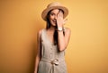 Young beautiful brunette woman on vacation wearing casual dress and hat covering one eye with hand, confident smile on face and Royalty Free Stock Photo