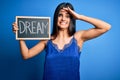 Young beautiful brunette woman wearing blue lingerie holding blackboard with dream message stressed with hand on head, shocked Royalty Free Stock Photo