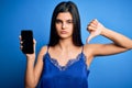 Young beautiful brunette woman wearing blue lingerie holding smartphone showing screen with angry face, negative sign showing Royalty Free Stock Photo