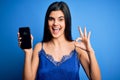 Young beautiful brunette woman wearing blue lingerie holding smartphone showing screen doing ok sign with fingers, excellent Royalty Free Stock Photo