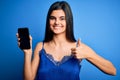 Young beautiful brunette woman wearing blue lingerie holding smartphone showing screen happy with big smile doing ok sign, thumb Royalty Free Stock Photo