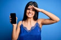 Young beautiful brunette woman wearing blue lingerie holding smartphone showing screen stressed with hand on head, shocked with Royalty Free Stock Photo